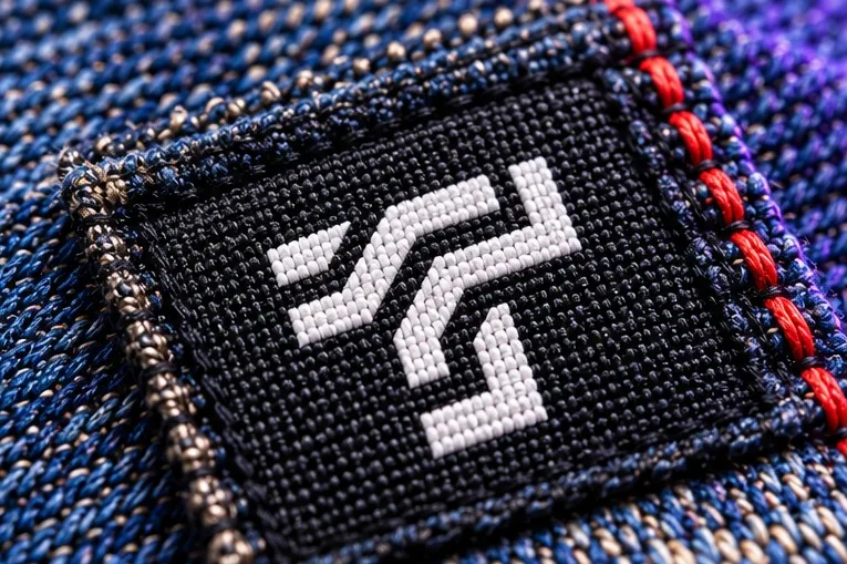 Macro of a black woven ThreadTap label stitched onto denim with red thread